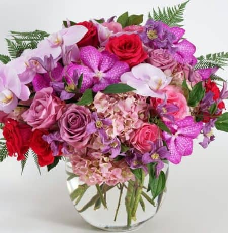 This stunning arrangement features soft pink phalaenopsis orchids cascading from a lush collection of pink hydrangea, lavender roses, and purple vanda orchids. Artfully accented with delicate touches of clematis and textural ferns, 