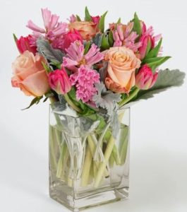 Brimming with beauty, this petite collection of pink and peach tones is sure to excite the senses. Fragrant hyacinth are nestled amidst peach roses and pink tulips and accented with delicate touches of dusty miller.