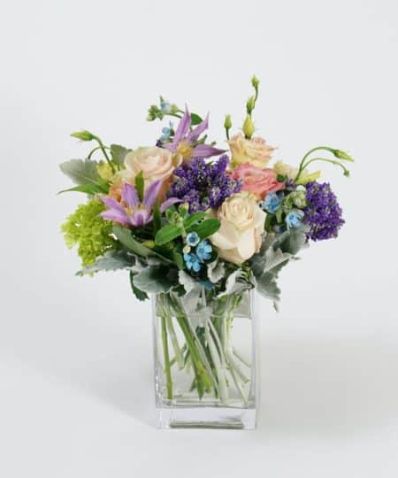 Filled with sweet summer tones, this beautiful collection of seasonal blooms includes pink lisianthus, blush roses, and mini green hydrangea with delicate accents of clematis, tweedia and veronica arranged in a clear glass vase.